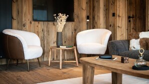 A modern living room with two white armchairs, a wooden coffee table, a small side table with a vase and books, and a grey sofa with a fur throw.