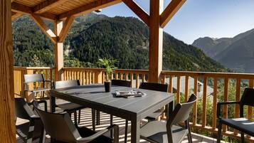 Een houten terras met een tafel en stoelen, met uitzicht op een bergachtig landschap.