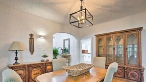 Un coin repas comprenant une table en bois, des chaises, un bol décoratif, un meuble avec des portes en verre et un luminaire suspendu.
