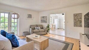 Un salon spacieux comprenant un canapé, une table basse et un téléviseur. Une porte donne accès à une autre pièce, et une fenêtre offre une vue sur la verdure environnante.