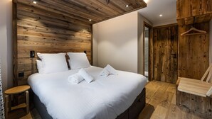 A bedroom with a wooden headboard, a bed with white linens, a wooden nightstand, and a wooden wardrobe.