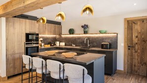 A modern kitchen with a central island, bar stools, wooden cabinets, and pendant lighting.