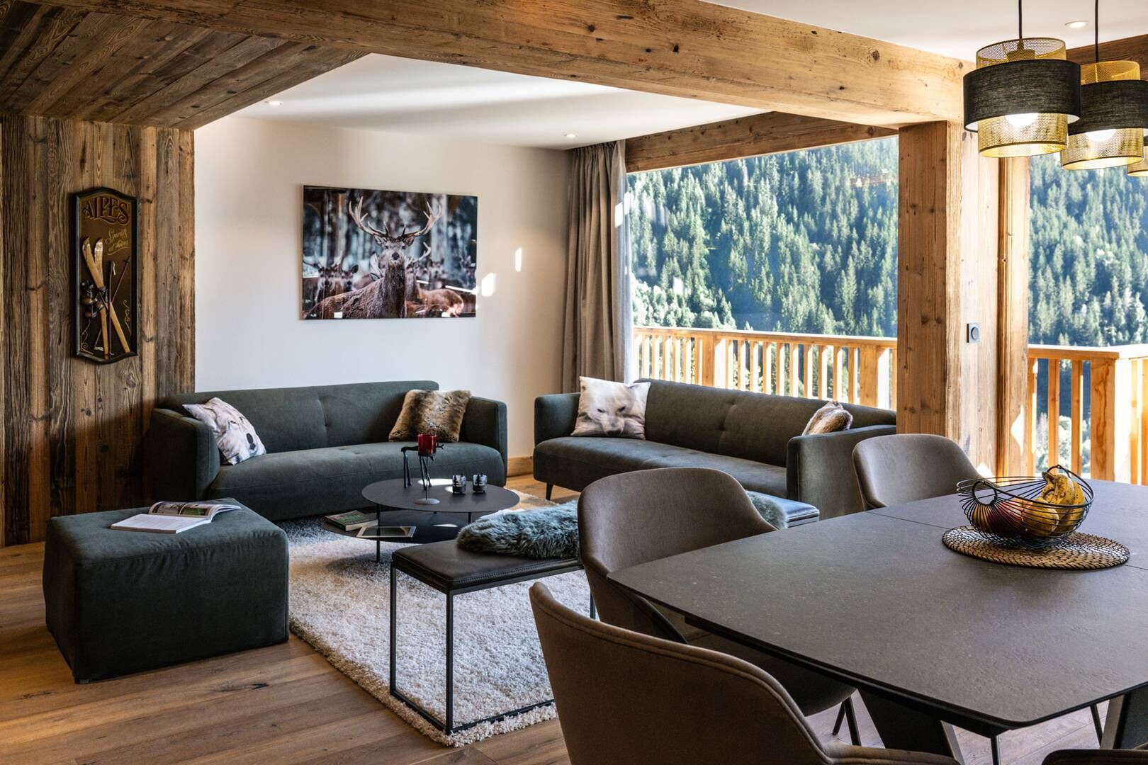 Un accogliente soggiorno con divano, tavolino e tavolo da pranzo. Una pittura adorna la parete, e ampie finestre offrono vista su una foresta.