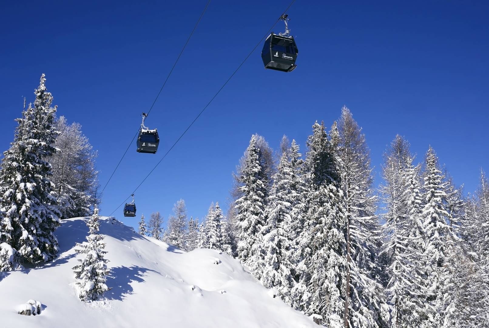 A ski lift with cabins moving along a snowy slope, surrounded by snow-covered trees.