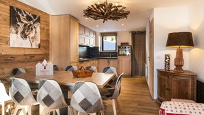 A dining area with a wooden table and chairs, a kitchen in the background, and a unique wooden chandelier. - N°10 : 10 people flat incl. swimmingpool, sauna, hammam (CHAMPAGNY EN VANOISE)