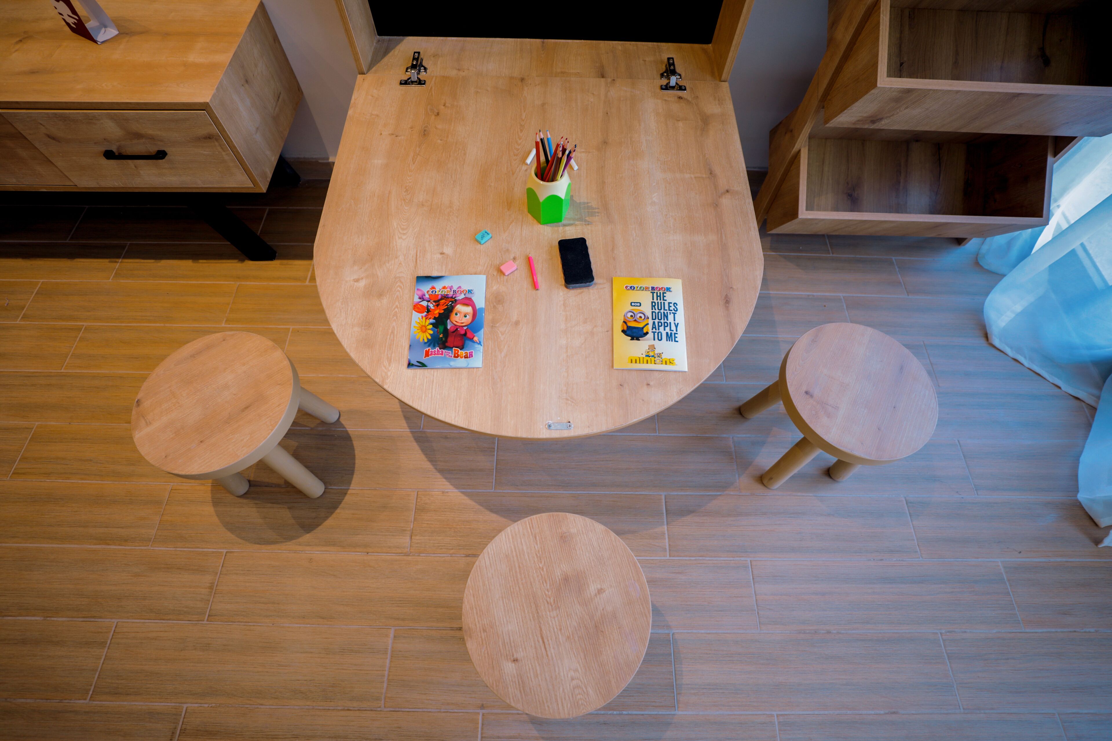 Una mesa de madera con dos taburetes, un teléfono inteligente y libros infantiles.