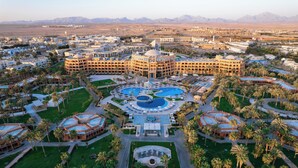 Un hotel grande con varias edificaciones, un patio central con piscinas y palmeras circundantes.