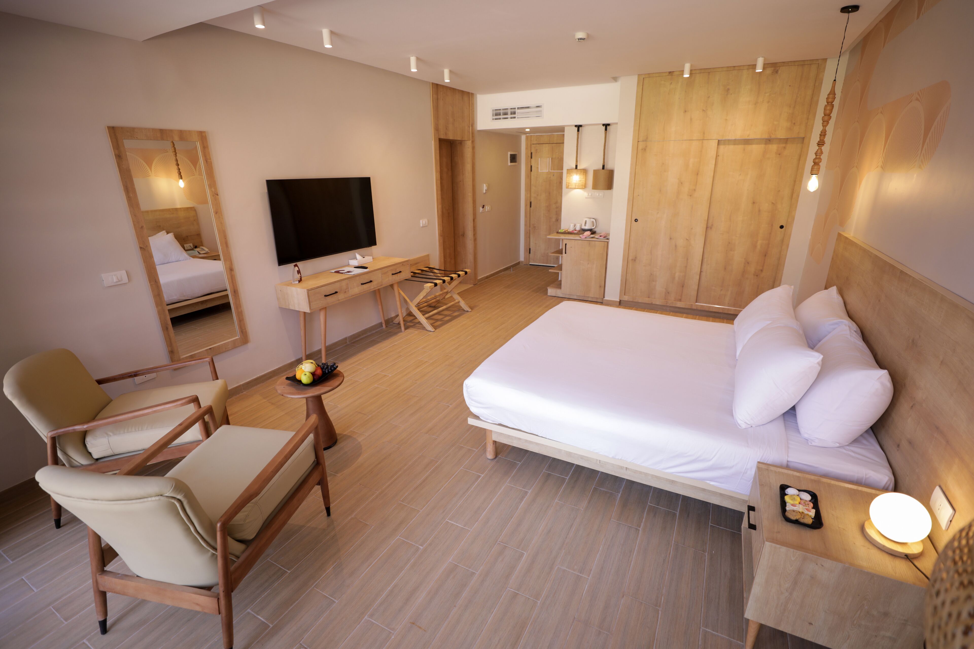 A modern hotel room with a large bed, a desk, a chair, a TV, and a wardrobe.