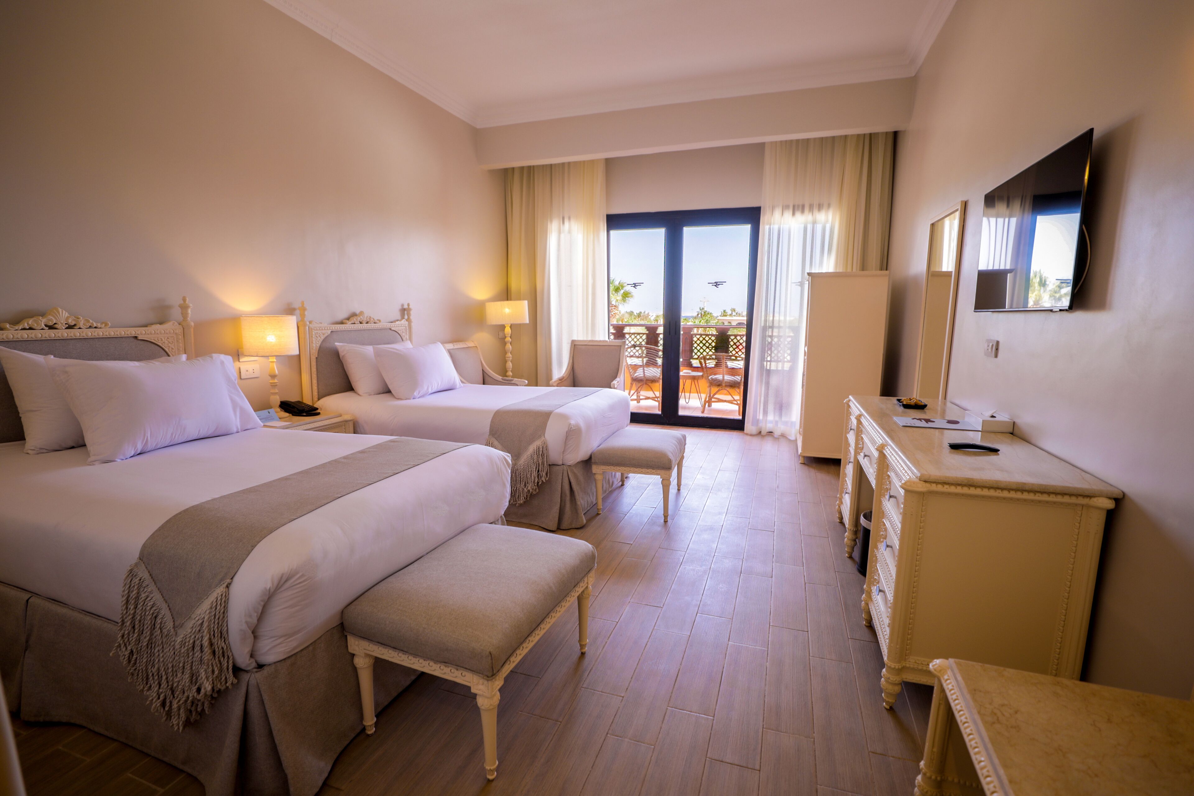 Een hotelkamer met twee bedden, een balkon, een televisie en een dressoir.