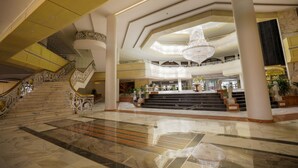 Un lobby espacioso con piso de mármol, una escalera central y una gran araña.