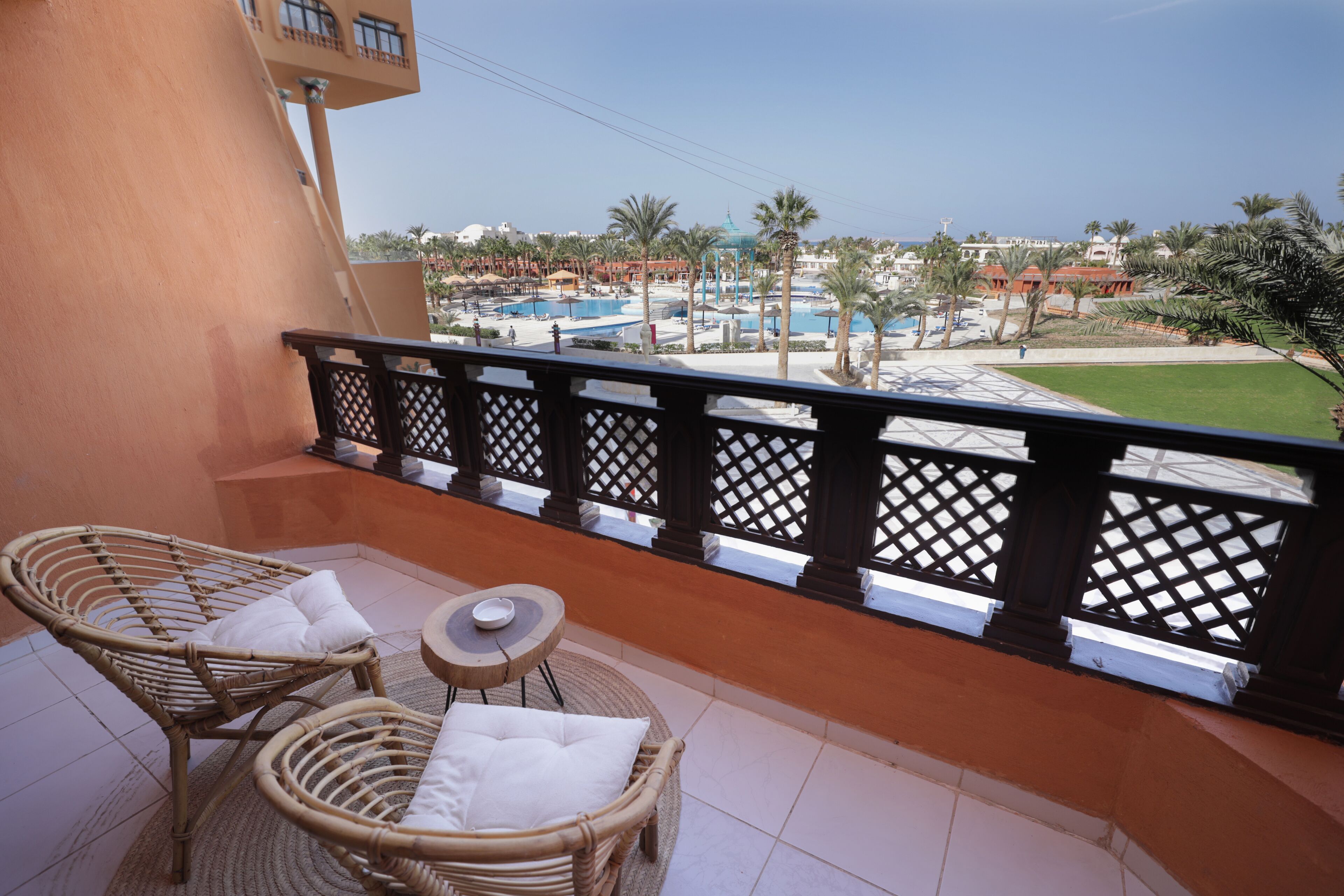 Un balcón con muebles de mimbre y vistas a una piscina y palmeras.