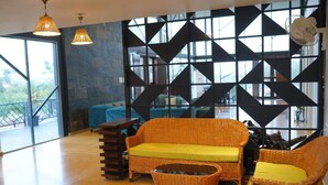 A spacious room with a large window, wicker furniture, and a geometric wall design. - Bliss Farm Stay-JASMINE (Amangal)