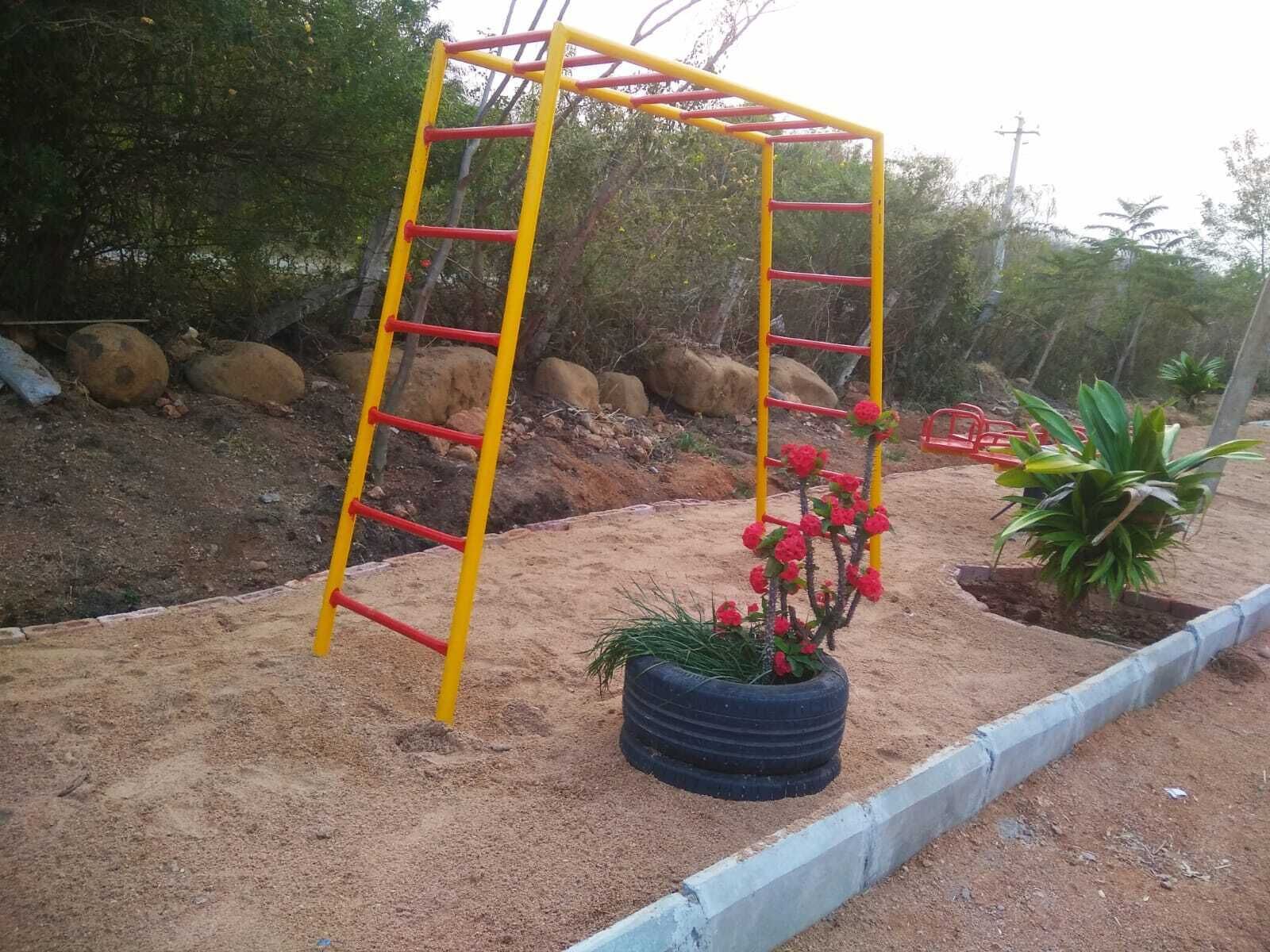 A playground with a yellow and red ladder structure, surrounded by sand and rocks.