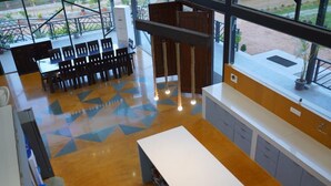A modern kitchen with a central island, a dining area with chairs, and a view through large windows. - Bliss Farm Stay-JASMINE (Amangal)