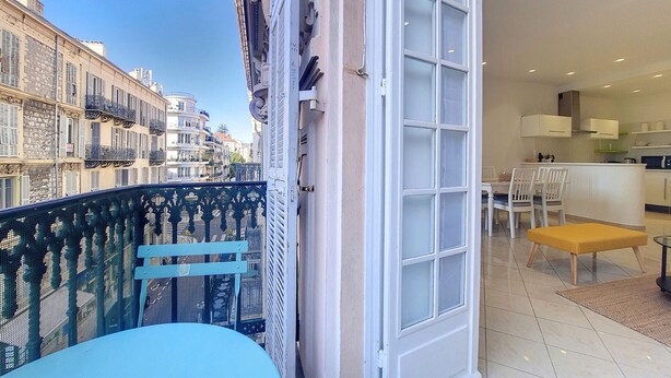 A balcony with a blue chair, a white door leading to a kitchen area with a dining table and chairs, and a view of neighboring buildings. - N&J - JACARANDA- Central, very close sea (Niza)
