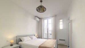 A bedroom with a bed, bedside tables, a hanging light fixture, a window with curtains, and a radiator. - N&J - JACARANDA- Central, very close sea (Niza)