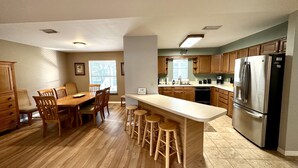 A kitchen with wooden cabinets, a stainless steel refrigerator, a dining table with chairs, and a bar area with stools. - House on Canal access to Lake! (Okeechobee)