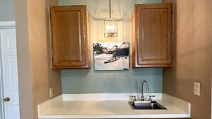 A compact kitchen with wooden cabinets, a white countertop, and a hanging pendant light. - House on Canal access to Lake! (Okeechobee)