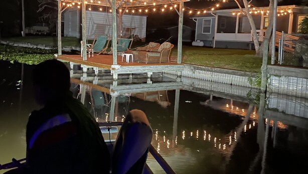 A covered outdoor seating area with string lights, a pool, and a small building in the background. - House on Canal access to Lake! (Okeechobee)