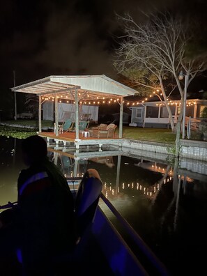 A covered outdoor seating area with string lights, a pool, and a small building in the background. - Water view Home with Dock on Canal with access to Lake! (Okeechobee)