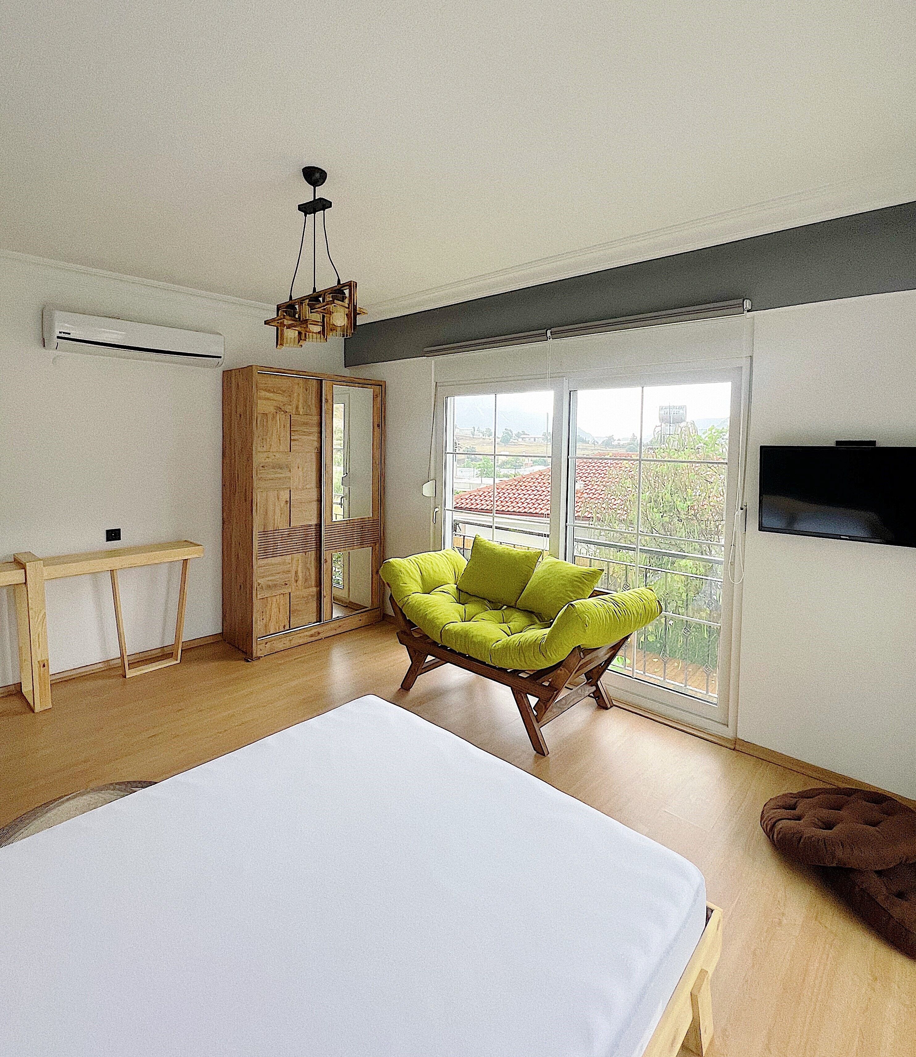 Een slaapkamer met een groot bed, een groene stoel, een houten garderobe en een televisie aan de muur.