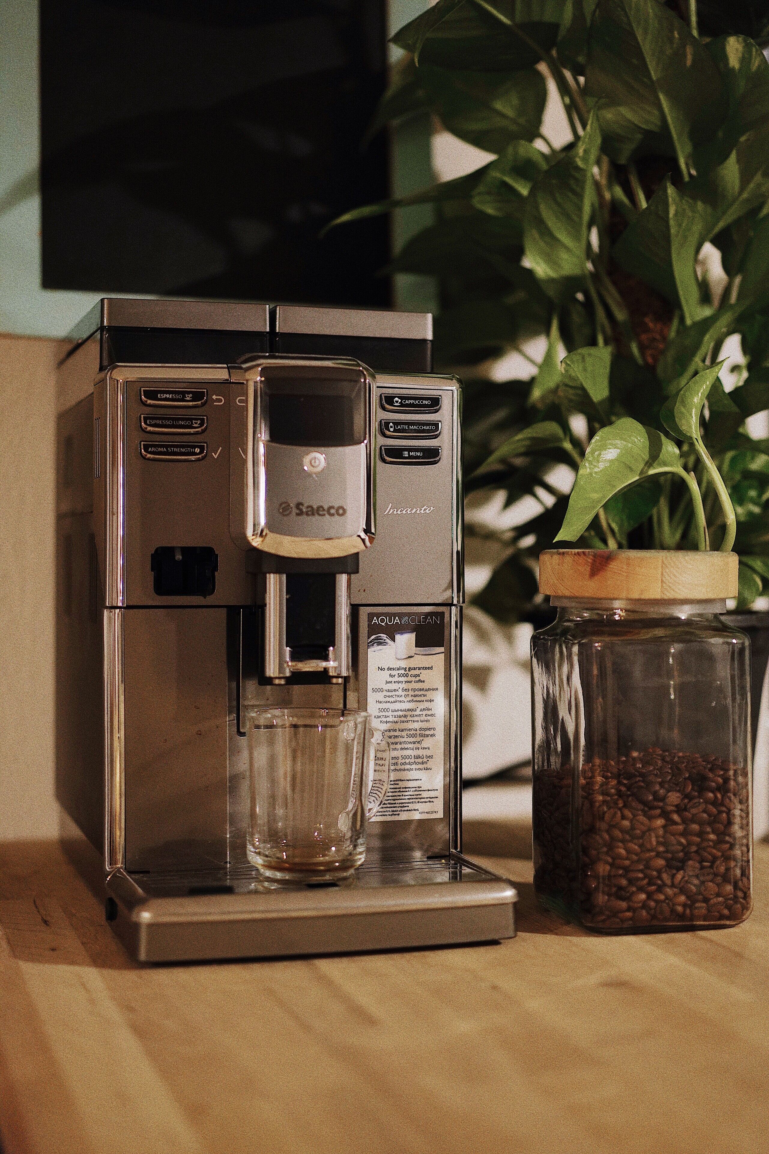 A Saeco espresso machine with a glass carafe and a jar of coffee beans.