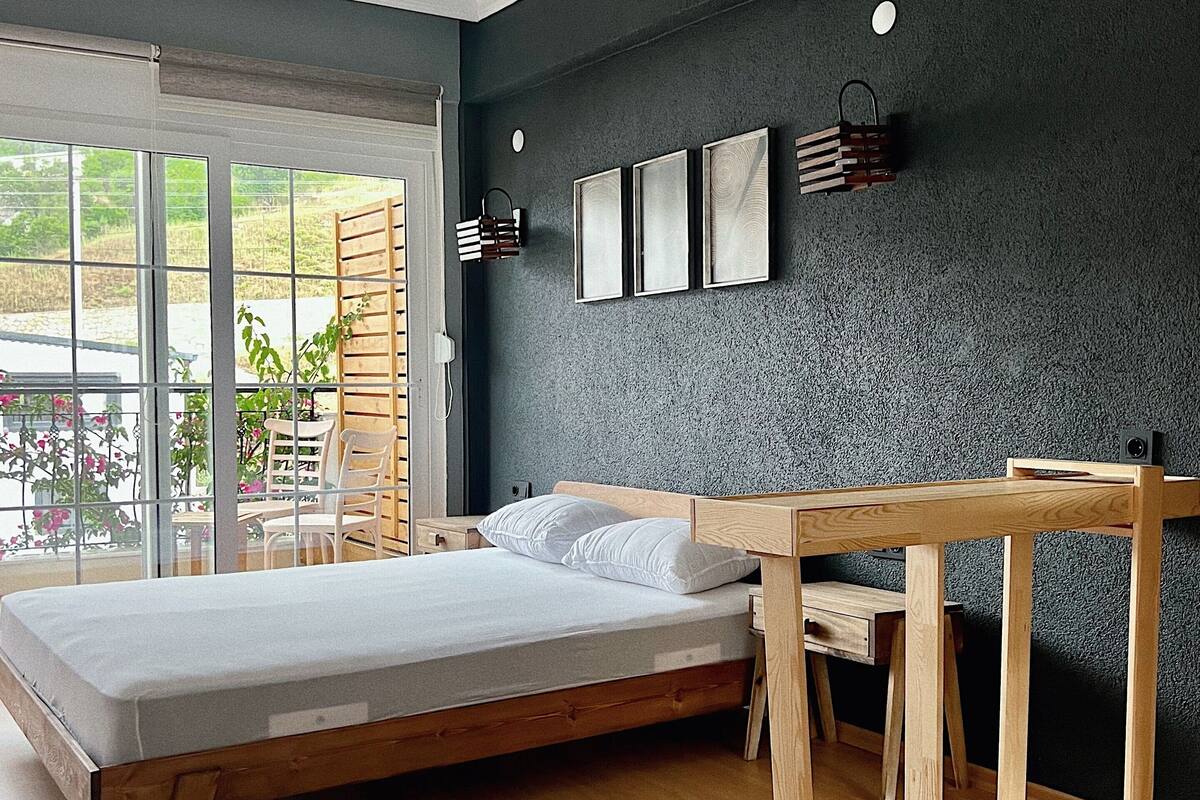Un dormitorio moderno con una cama grande, muebles de madera, un escritorio y vistas a través de una puerta corrediza de vidrio.