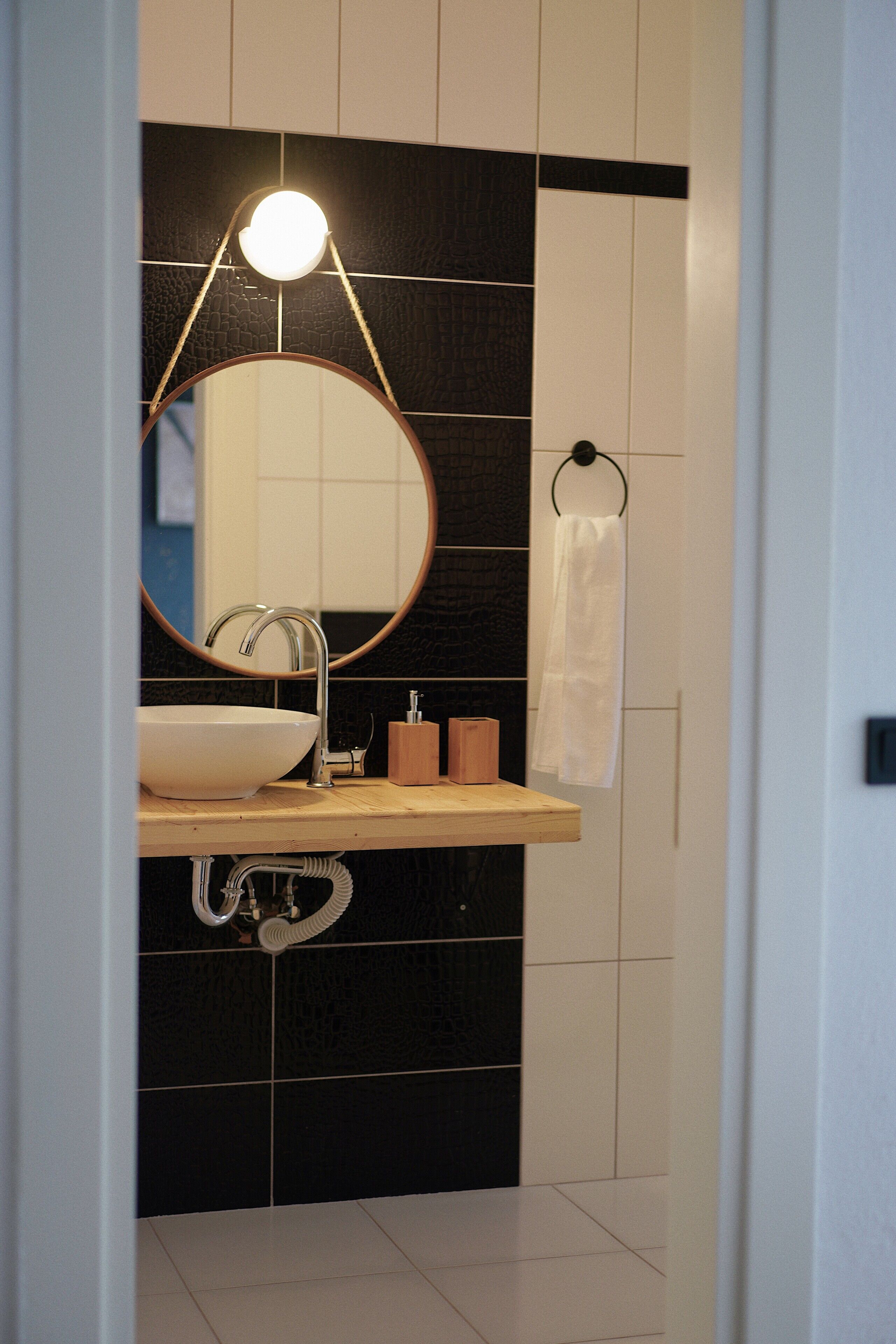 Un baño con un espejo redondo, un lavabo, un perchero para toallas y un dispensador de jabón.