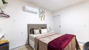 Quarto com cama, planta pendente, ar-condicionado e porta.