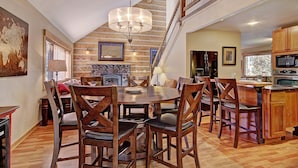 A dining area with a wooden table and chairs, a chandelier, a fireplace, and a kitchen with modern appliances. - Ziggy Bear Lodge (Breckenridge)