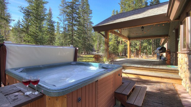 A hot tub with two glasses of red wine, a wooden bench, and a covered patio area with a barbecue grill. - Ziggy Bear Lodge (Breckenridge)