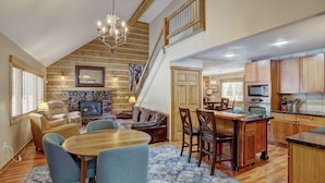 A spacious living area with a fireplace, a dining table with chairs, a kitchen with wooden cabinets, and a staircase leading to an upper level. - Ziggy Bear Lodge (Breckenridge)