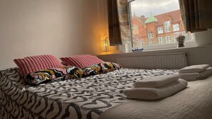 Ein Schlafzimmer mit Bett, Kissen, einem Fenster mit Blick auf Gebäude und einem Gemälde an der Wand.