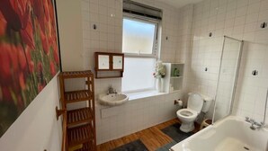 Ein Badezimmer mit Waschbecken, Toilette und Badewanne. Ein Fenster bietet einen Ausblick nach draußen.