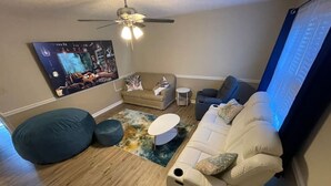 A living room with a beige sofa, a blue bean bag, a white coffee table, and a ceiling fan.