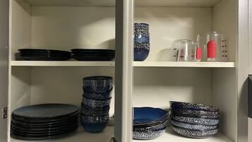 A kitchen cabinet with shelves holding black plates, blue and white patterned bowls, and clear measuring cups with red lids.