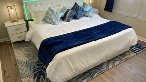 A neatly made bed with a white and blue color scheme, a bedside table with a lamp, and a patterned rug on a wooden floor.