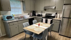 A modern kitchen with grey cabinets, a wooden dining table with placemats, two grey chairs, and a stainless steel refrigerator.