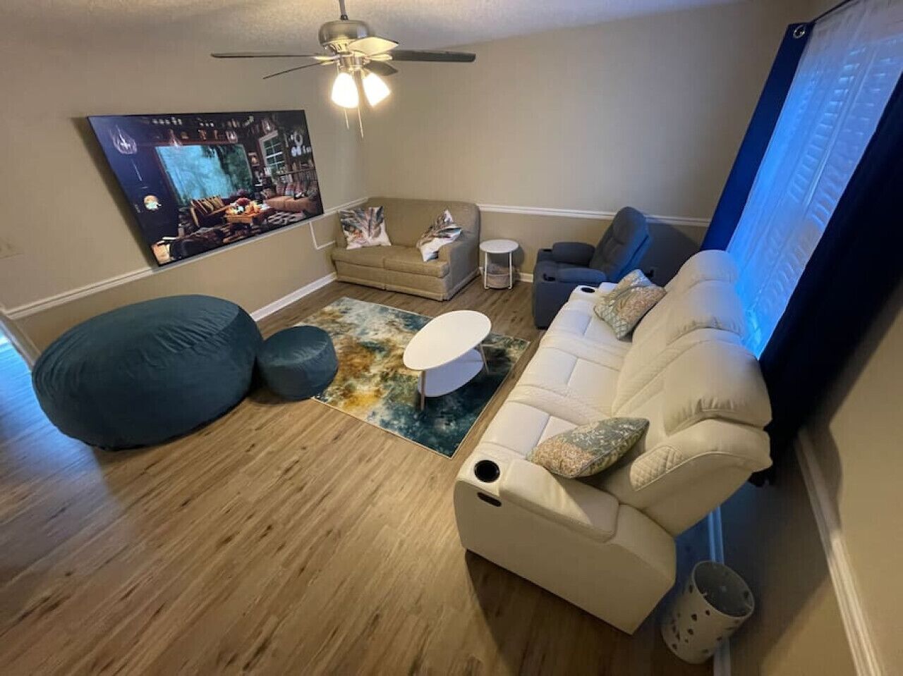 A living room with a beige sofa, a blue bean bag, a white coffee table, and a ceiling fan.