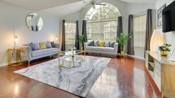 A spacious living room with hardwood flooring, a marble-patterned rug, two sofas with cushions, a coffee table, and a large window with curtains. - Kissimmee Condo w/ Perks: 6 Mi to Disney World! (Kissimmee)