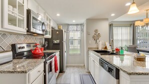 A modern kitchen with white cabinetry, granite countertops, stainless steel appliances, and a window with a view. - Kissimmee Condo w/ Perks: 6 Mi to Disney World! (Kissimmee)