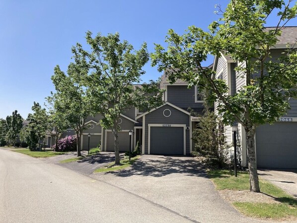 A row of townhouses with attached garages, a clear driveway, and mature trees.