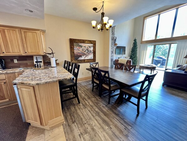 A spacious kitchen with wooden cabinets, a granite countertop, and a dining area with a large table and chairs. - Seven Springs Condo Near Shuttle, Gas Fireplace (Champion)
