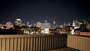 A nighttime cityscape with a view of illuminated buildings and a balcony railing.