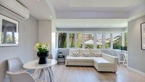 A modern living room with a white sofa, a glass table, and a potted plant.