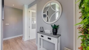 A hallway with a grey wall, a white console table with drawers, a round mirror, and a potted plant.