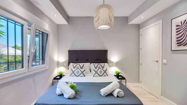 A modern bedroom with a large bed, a dark headboard, and a hanging light fixture.