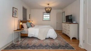 A bedroom with a bed, bedside table, lamp, dresser, TV, and a chandelier. - Spacious 3BD 2BA w/fenced yard & direct bike trail access. Near GVL, TR, Furman. (Greenville)
