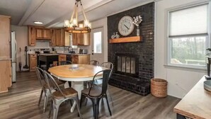 A kitchen with wooden cabinets, a round dining table with chairs, a chandelier, and a fireplace with a clock. - Spacious 3BD 2BA w/fenced yard & direct bike trail access. Near GVL, TR, Furman. (Greenville)