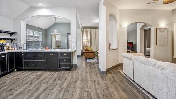 A modern kitchen with dark cabinets, a central island, and a dining area with a sofa and a TV.